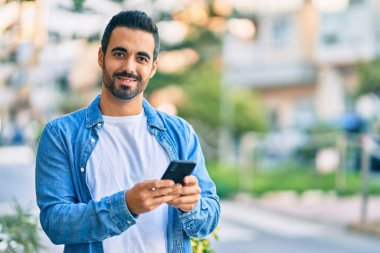 Genç İspanyol adam şehirde akıllı telefon kullanarak mutlu gülümsüyor..