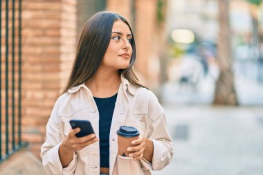 Akıllı telefon kullanan ve şehirde kahve içen ciddi bir suratı olan genç İspanyol kız..