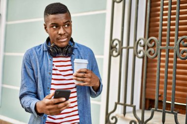 Genç Afrikalı Amerikalı adam akıllı telefon kullanıyor. Şehirde kahve içiyor..