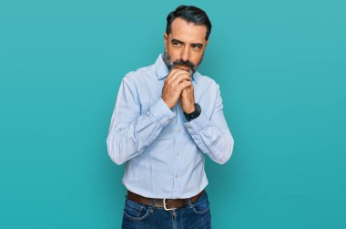 Orta yaşlı, sakallı, iş gömleği giyen, gergin ve heyecanlı bir adam elleri çenesinde yan tarafa bakıyor. 