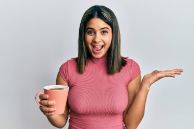 Genç Latin kadın kahveyle zaferi kutluyor mutlu bir gülümsemeyle ve kazanan el kaldırarak. 