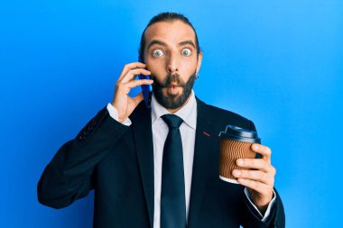 Uzun saçlı ve sakallı çekici bir iş adamı akıllı telefon kullanıyor ve bir fincan kahve içiyor. Ağızlı balık suratı yapıyor ve şaşı bakıyor. Deli ve komik.. 