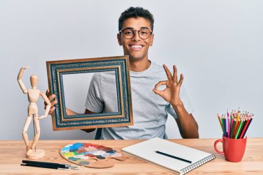Genç ve yakışıklı Afrikalı Amerikalı ressam sanat stüdyosunda boş bir çerçeve tutuyor. Parmaklarıyla işaret veriyor, gülümsüyor. Mükemmel bir sembol. 