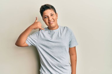 Gündelik gri tişört giyen genç İspanyol çocuk telefonla el ve parmak hareketleriyle gülümsüyor telefonda konuşur gibi. iletişim kavramları. 