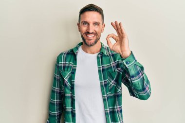 Sakallı, sıradan kıyafetler giyen, olumlu gülümseyen, el ve parmaklarıyla 