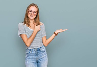 Güzel, genç, sarışın bir kadın gündelik kıyafetler ve gözlük takıyor kameraya hayret ediyor ve gülümsüyor.. 