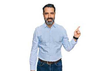 Sakallı, iş gömleği giyen, yüzünde kocaman bir gülümseme olan orta yaşlı bir adam. Elinle kameraya bakıyor.. 