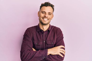 Gündelik kıyafetler giyen, kollarını kavuşturup kameraya gülümseyen genç İspanyol adam. pozitif kişi. 