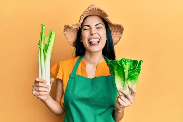 美しい若い女性を身に着けている庭師エプロン保持野菜ステッキング舌アウト幸せな面白い式 — ストック写真