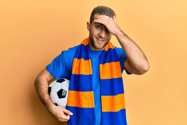 若いです白人男性サッカーウーリガン応援ゲーム保持ボールを強調し 頭の上に手で不満 驚きと怒っている顔 — ストック写真