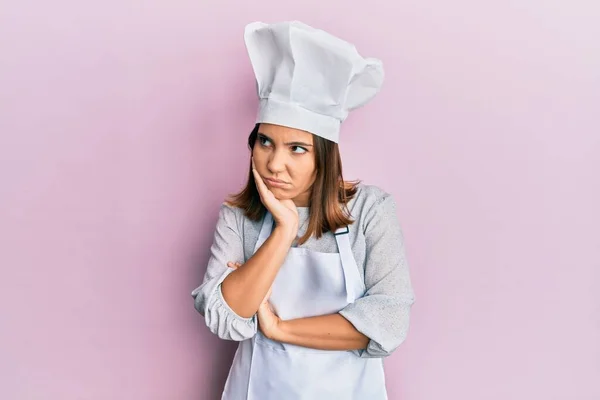 年轻美丽的女人穿着职业厨师制服 头戴帽子 看上去疲惫 对交叉双臂的忧郁症感到厌烦 — 图库照片
