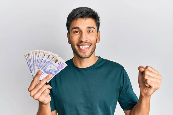 Joven Hombre Guapo Sosteniendo Billetes Coronas Suecas Gritando Orgulloso Celebrando —  Fotos de Stock