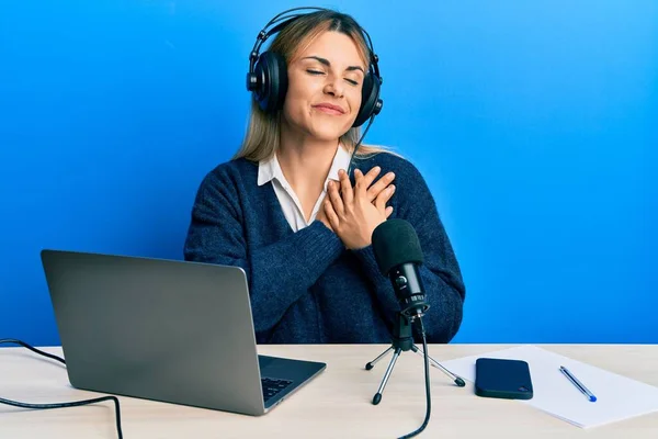 年轻的高加索女人在电台演播室工作 双手放在胸前微笑 满脸感激地闭上眼睛 健康概念 — 图库照片