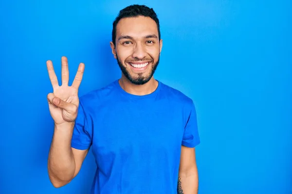 自信と幸せ笑みを浮かべている間 髭を生やしたヒスパニック系の男は カジュアルな青のTシャツを着て指の数3を示すと指摘 — ストック写真