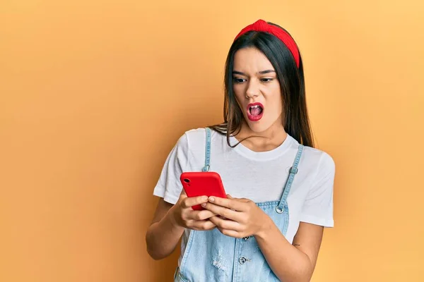 Young Hispanic Girl Using Smartphone Shock Face Looking Skeptical Sarcastic — Stock Photo, Image