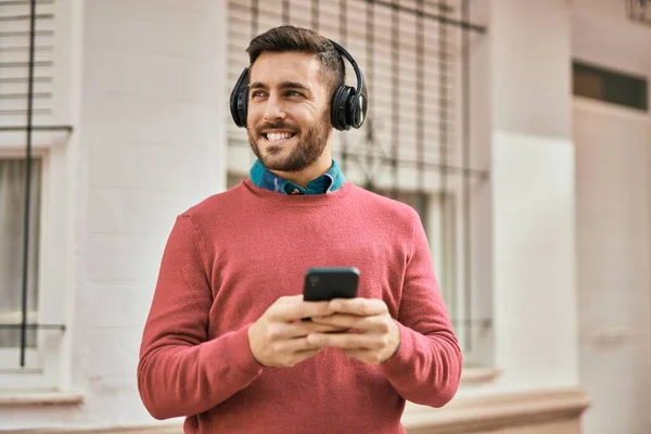 Joven Hombre Hispano Sonriendo Feliz Usando Teléfonos Inteligentes Auriculares Ciudad —  Fotos de Stock