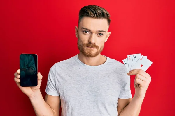 Homem Ruivo Jovem Segurando Smartphone Cartão Casino Relaxado Com Expressão — Fotografia de Stock