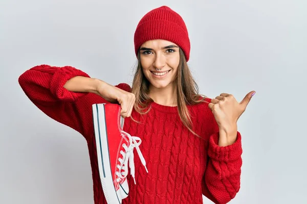 Jovem Hispânica Segurando Sapatos Casuais Vermelhos Apontando Polegar Para Lado — Fotografia de Stock