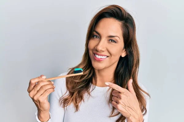 年轻的拉丁女人拿着牙刷 牙膏微笑着 高兴地用手和手指指指点点 — 图库照片