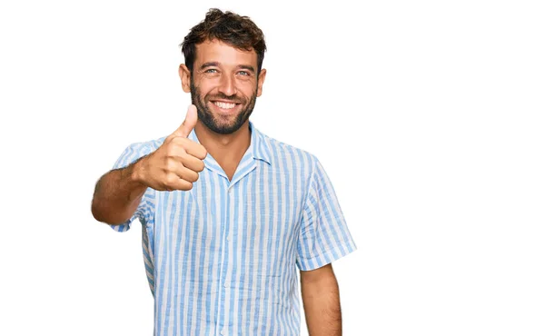 英俊的年轻男子留着胡子 穿着休闲的新鲜衬衫 手拿着快乐的大拇指做手势 赞成的表情看着相机显示的成功 — 图库照片