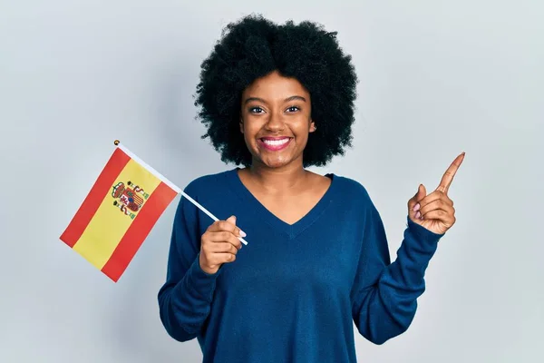 年轻的非洲裔美国女人拿着西班牙国旗 高兴地微笑着 手指手画脚地指向一边 — 图库照片