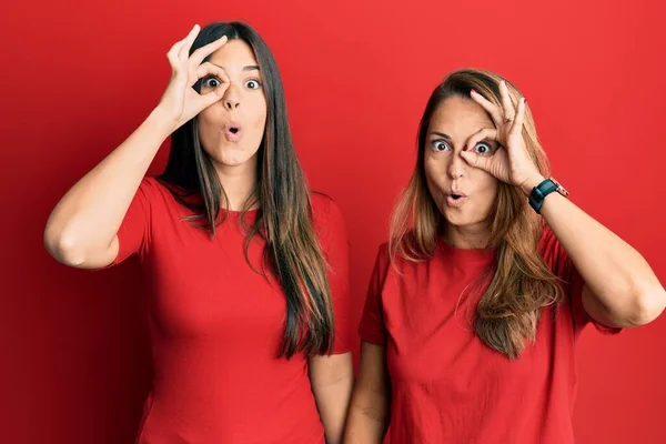 西班牙裔家庭的母亲和女儿穿着红色背景的休闲装 摆出一副惊讶的样子 用手指看着对方 不信的表情 — 图库照片