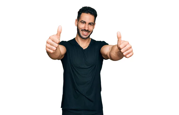 留着胡子的西班牙裔男人穿着宽松的黑色T恤 肯定用手做积极的手势 微笑着竖起大拇指 为成功感到高兴 优胜手势 — 图库照片