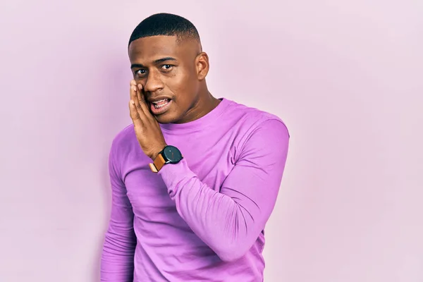 若いです黒男身に着けていますカジュアルなピンクのセーター手で口から秘密の噂を伝えます ささやき悪意のある話 — ストック写真