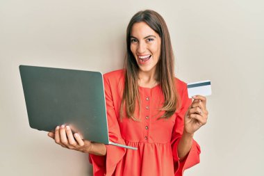 Genç, güzel bir kadın dizüstü bilgisayar ve kredi kartı tutuyor ve kahkahalarla gülüyor.. 