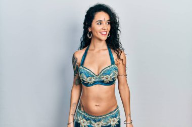 Bindi giyen ve geleneksel göbek dansı kıyafetleri giyen genç bir kadın yüzünde gülümsemeyle yan yana bakıyor, doğal bir ifade. Kendinden emin gülen. 