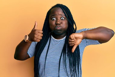 Örgülü genç siyahi kadın baş parmaklarını eğiyor ve komik yüzüyle yanaklarını şişiren jestleri onaylıyor. Ağzı havayla şişer, havayı yakalar.. 