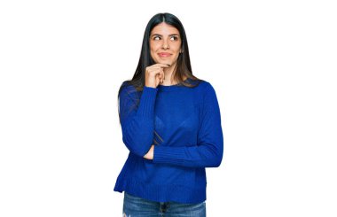 Elleri çenesinde gündelik kıyafetler giyen genç İspanyol kadın soru sormayı düşünüyor, düşünceli bir ifade. Düşünceli bir yüzle gülümsüyor. şüphe kavramı. 