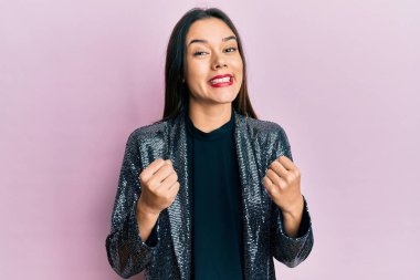 Parti ceketi giyen genç İspanyol kız şaşırmış ve şaşırmış bir şekilde kollarını kaldırarak ve gözlerini açarak başarıyı kutluyor. Kazanan konsept. 