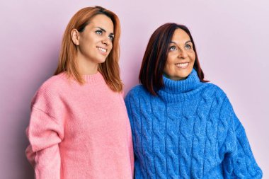 Latin anne ve kızı günlük giysiler giyip yan tarafa bakıyorlar, rahat profil pozu veriyorlar doğal bir yüz ve kendinden emin bir gülümsemeyle.. 