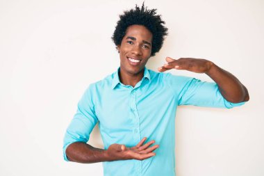 Yakışıklı Afro saçlı, sıradan kıyafetler giyen, büyük ve büyük boy işareti gösteren, ölçü sembolü olan Afro Amerikalı bir adam. Kameraya bakıp gülümsüyor. ölçüm kavramı. 