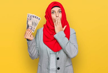Güzel İspanyol kadın, elinde Japon yen banknotları tutan, ağzı elle kapatan, şok olmuş ve hata yapmaktan korkan, İslamcı başörtüsü takıyor. şaşırmış ifade 