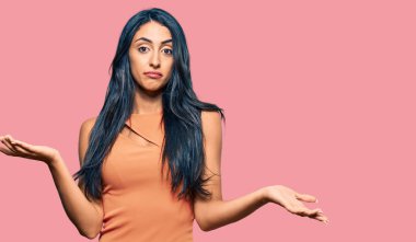 Yazlık elbise giyen güzel İspanyol kadın elleri ve kolları havada, kafası karışık bir ifade takınıyor. şüphe kavramı. 