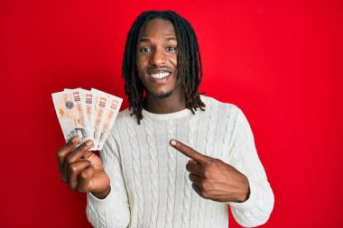Saçları örgülü Afrika kökenli bir Amerikalı elinde 10 pound banknotla mutlu mesut gülümsüyor. 