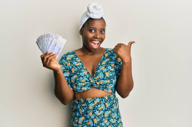 Kıllı türban takan genç Afrikalı bir kadın elinde 20 İsveç banknotuyla baş parmağını kaldırıp ağzı açık gülümsüyor. 