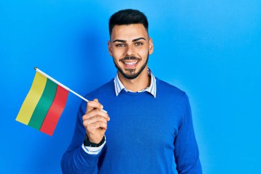 Litvanya bayrağı tutan sakallı genç İspanyol adam pozitif ve mutlu görünüyor ve kendine güvenen bir gülümsemeyle dişlerini gösteriyor. 