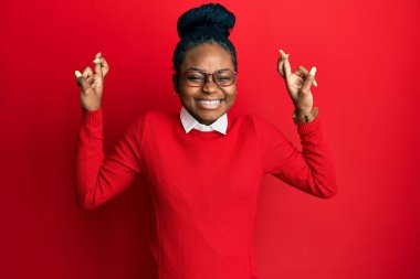 Sıradan kıyafetler ve gözlük takan Afro-Amerikalı genç bir kadın umut ve gözlerin kapalı bir şekilde gülümseyerek el sallıyor. Şans ve batıl inançlar. 