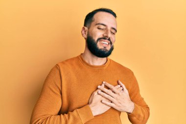 Sakallı, sıradan bir kazak giyen, elleri göğsünde, gözleri kapalı gülümseyen ve yüzünde minnet ifadesi olan genç bir adam. sağlık kavramı. 