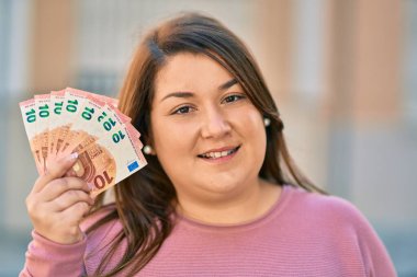 Genç İspanyol artı iri kadın gülümseyerek şehirde 10 avroluk banknotlar tutuyor..