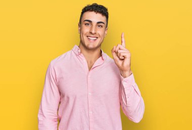 Gündelik kıyafetler giyen İspanyol genç adam başarılı bir fikirle işaret ediyor. Heyecanlı ve mutlu. Bir numara.. 