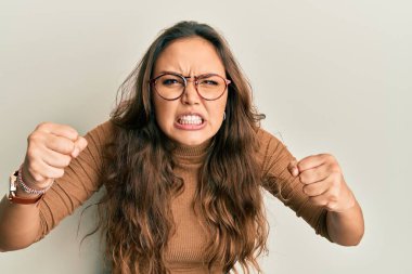 Gündelik kıyafetler giyen, gözlüklü kızgın ve kızgın genç İspanyol kız öfkeyle bağırırken kızgın ve öfkeli yumruklar sallıyor. öfke ve agresif konsept. 