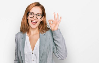 İş stili ve gözlüklü beyaz bir kadın gülümsüyor. El ve parmaklarıyla 