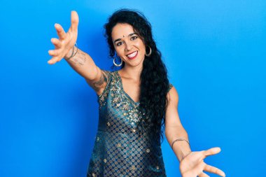 Bindi ve geleneksel kurta elbisesi giymiş genç bir kadın kameraya sarılıp gülümseyerek bakıyor. Mutluluğu kucaklayan neşeli bir ifade.. 