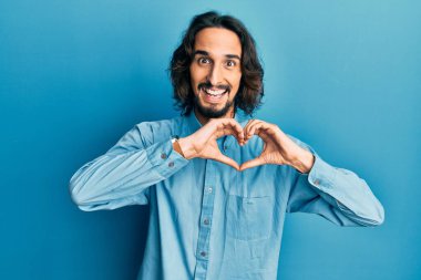 Gündelik kıyafetler giyen, aşık gülümseyen, elleriyle kalp sembolü yapan genç bir İspanyol. romantik kavram. 