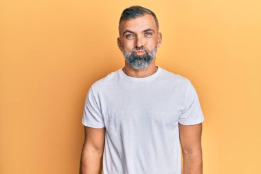 Sıradan beyaz tişört giyen, komik suratlı, yanakları şişen orta yaşlı yakışıklı bir adam. Havayla şişmiş ağız, çılgın bir ifade.. 