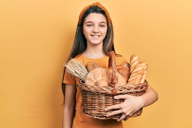 Genç esmer kız elinde hasırdan bir sepet tutarken pozitif ve mutlu görünüyor. Kendine güvenen bir gülümsemeyle dişlerini gösteriyor. 